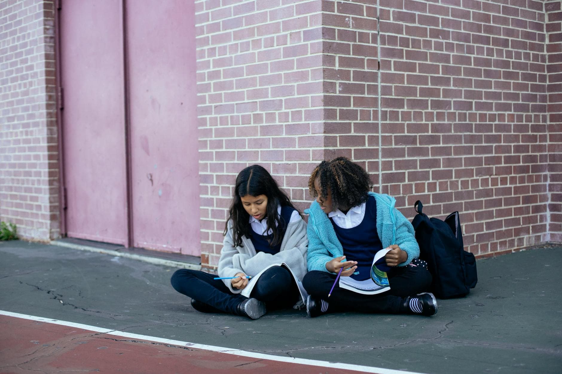 Two schoolgirls studying together outside in school uniforms.