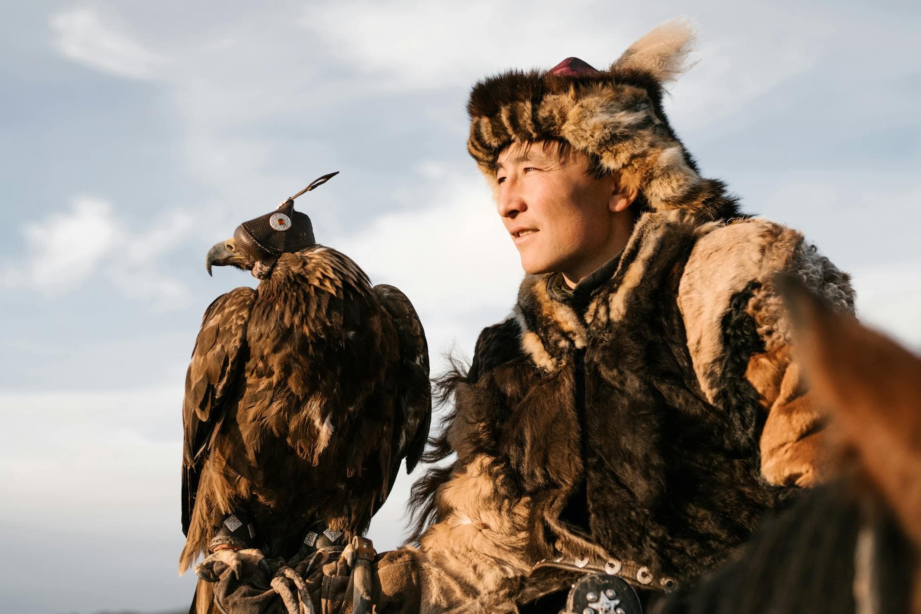 A traditional eagle hunter dressed in fur holding a trained golden eagle, representing ancient cultural practices.