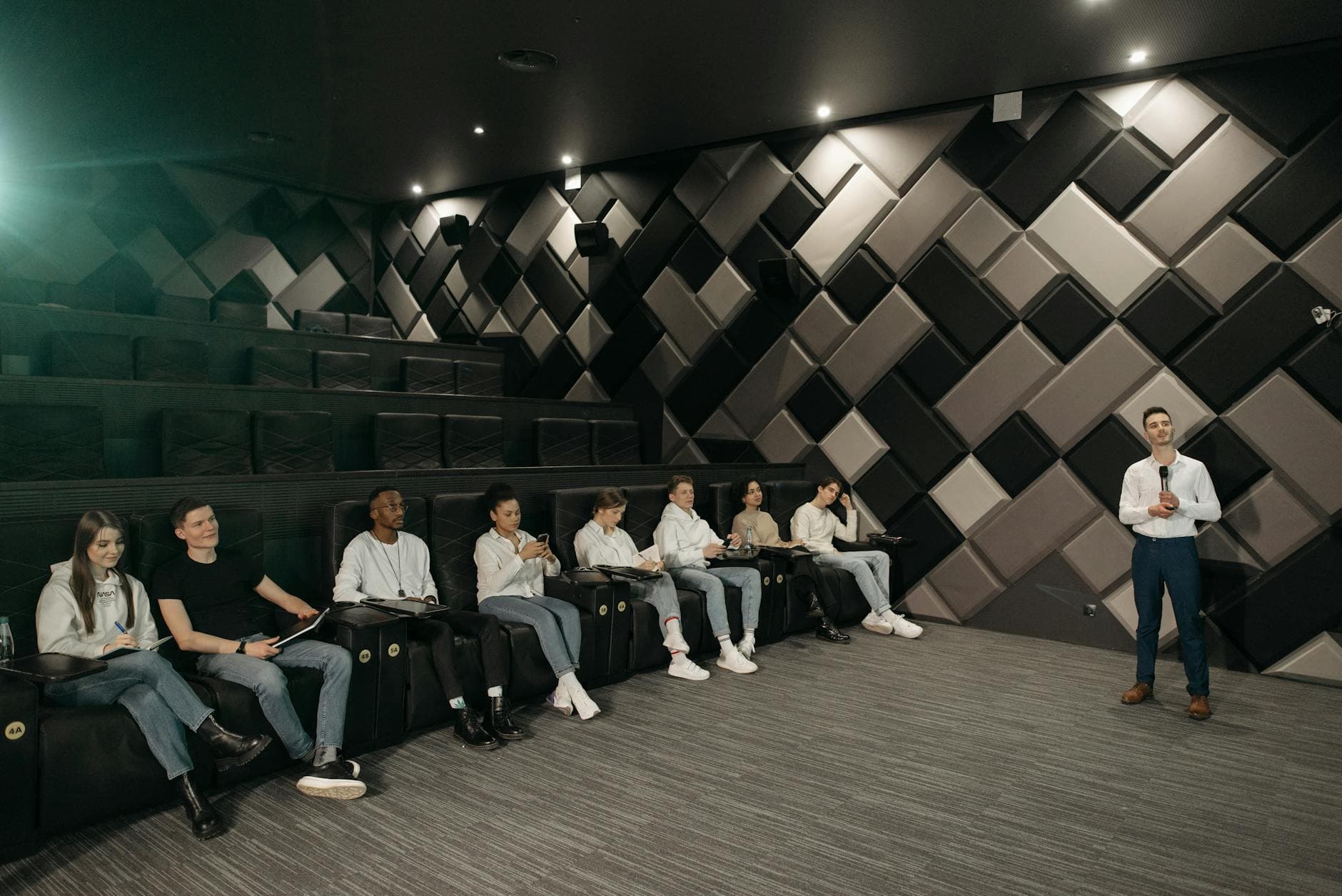 Speaker addressing a diverse audience in a modern theater setting.