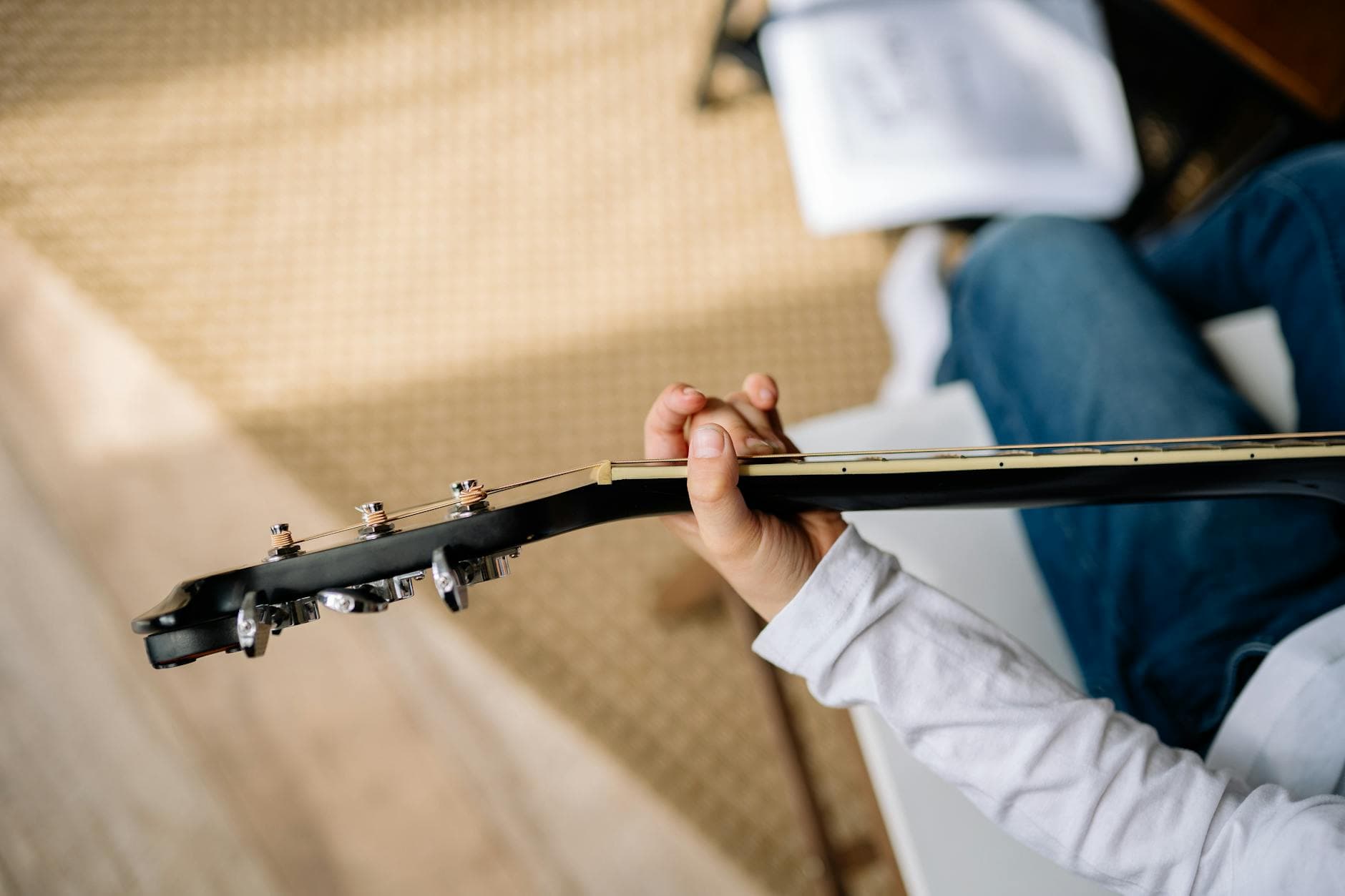 A person in white sleeves plays an acoustic guitar, focusing on hand technique.