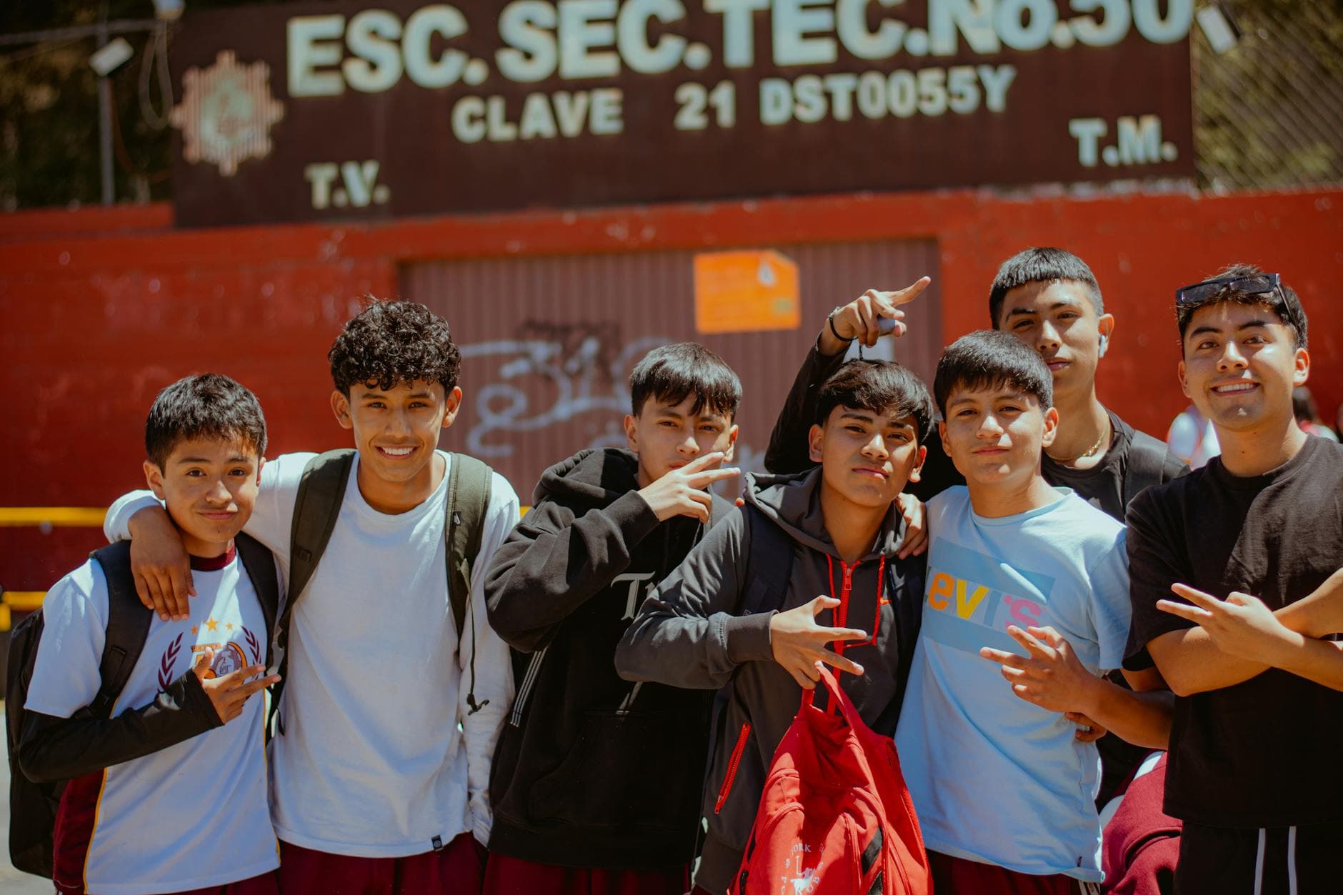 Teenagers posing for a group photo in front of a school building on a sunny day.