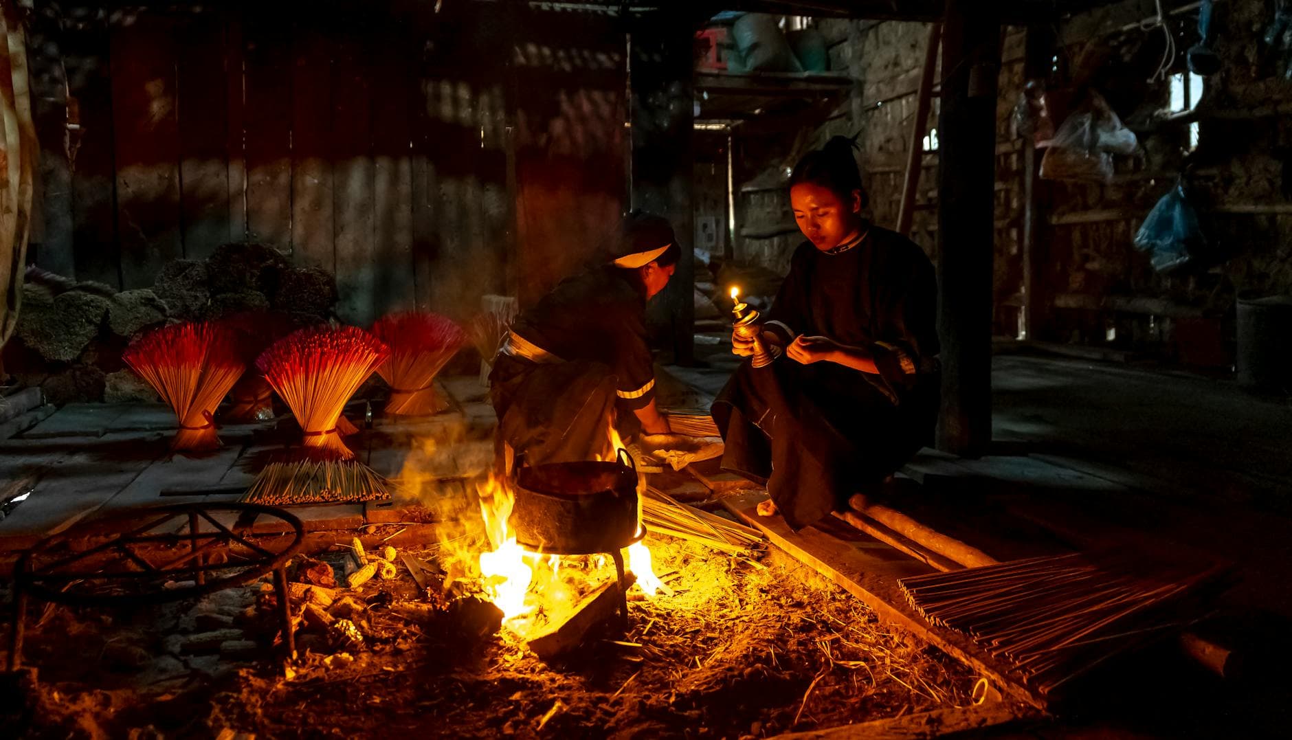 Two women making incense by firelight in a rustic workshop.