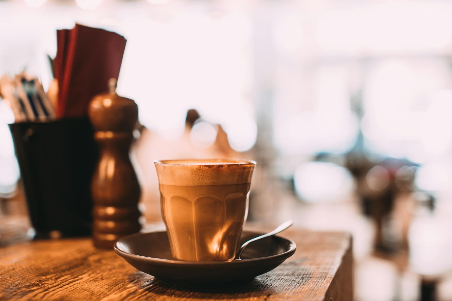 A warm cup of coffee on a saucer with a blurred cafe background captures cozy moments.