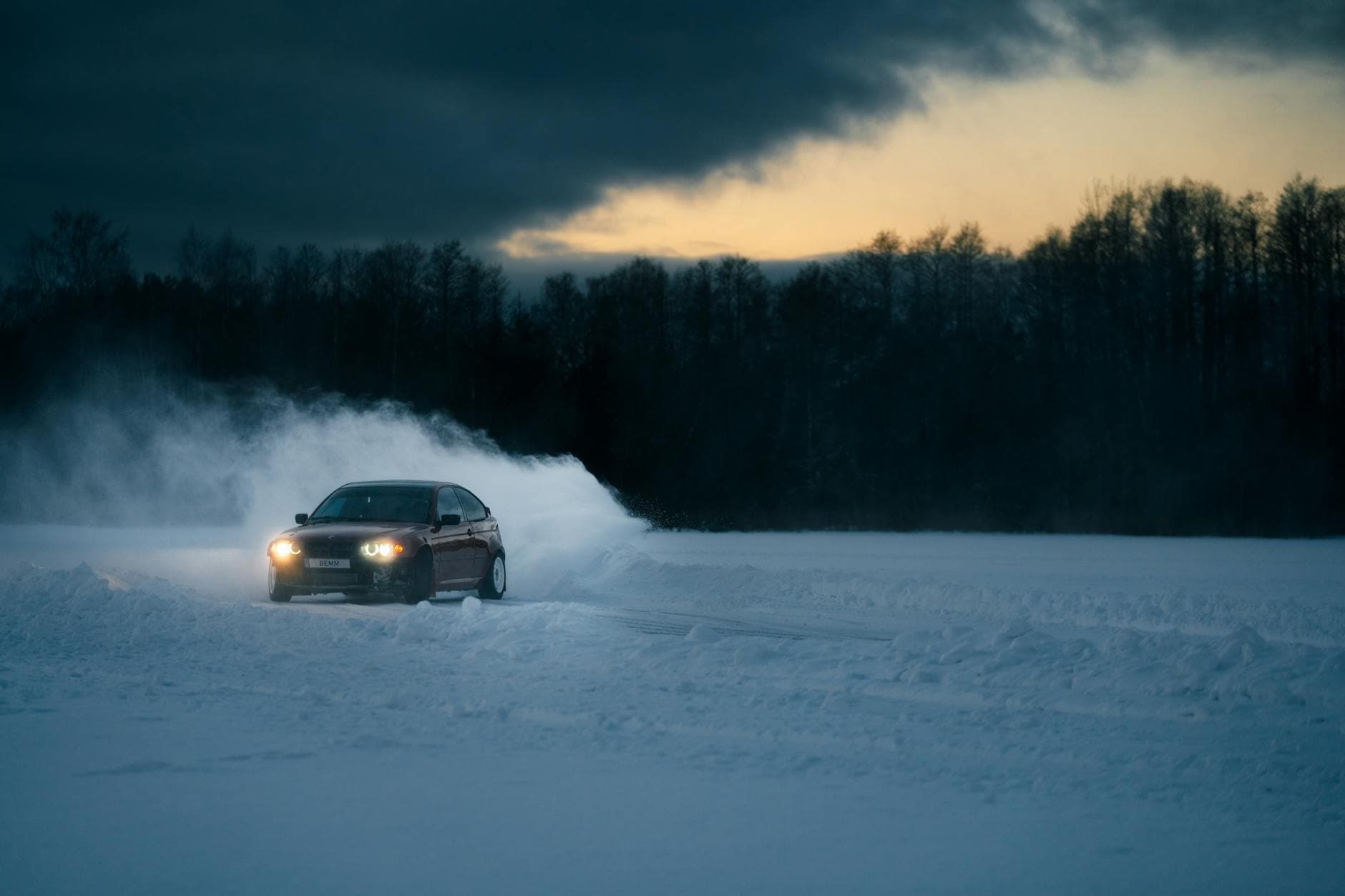 A car powerfully drifts through snow on a road at dusk, showcasing vibrant action and winter landscape.