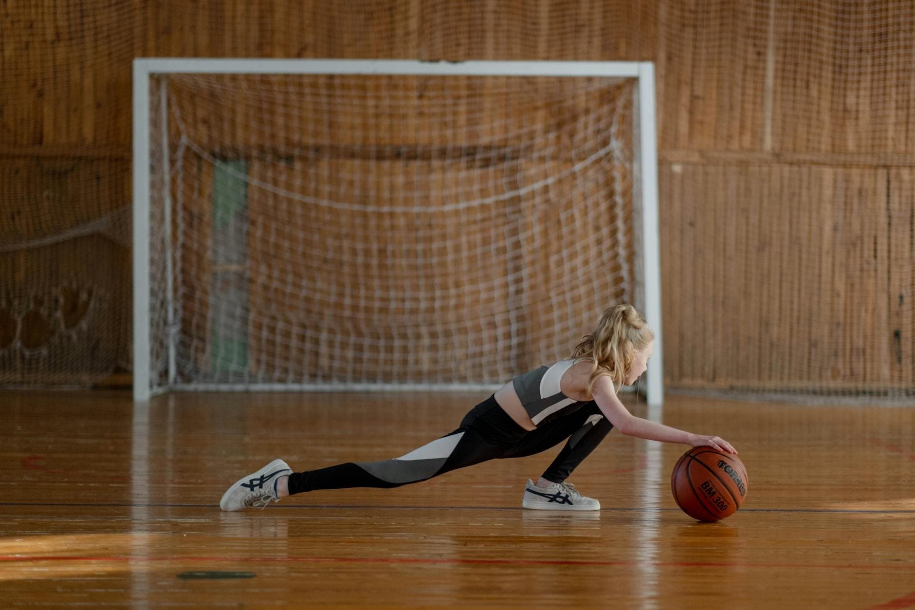 A young girl stretching with a basketball in an indoor sports hall.