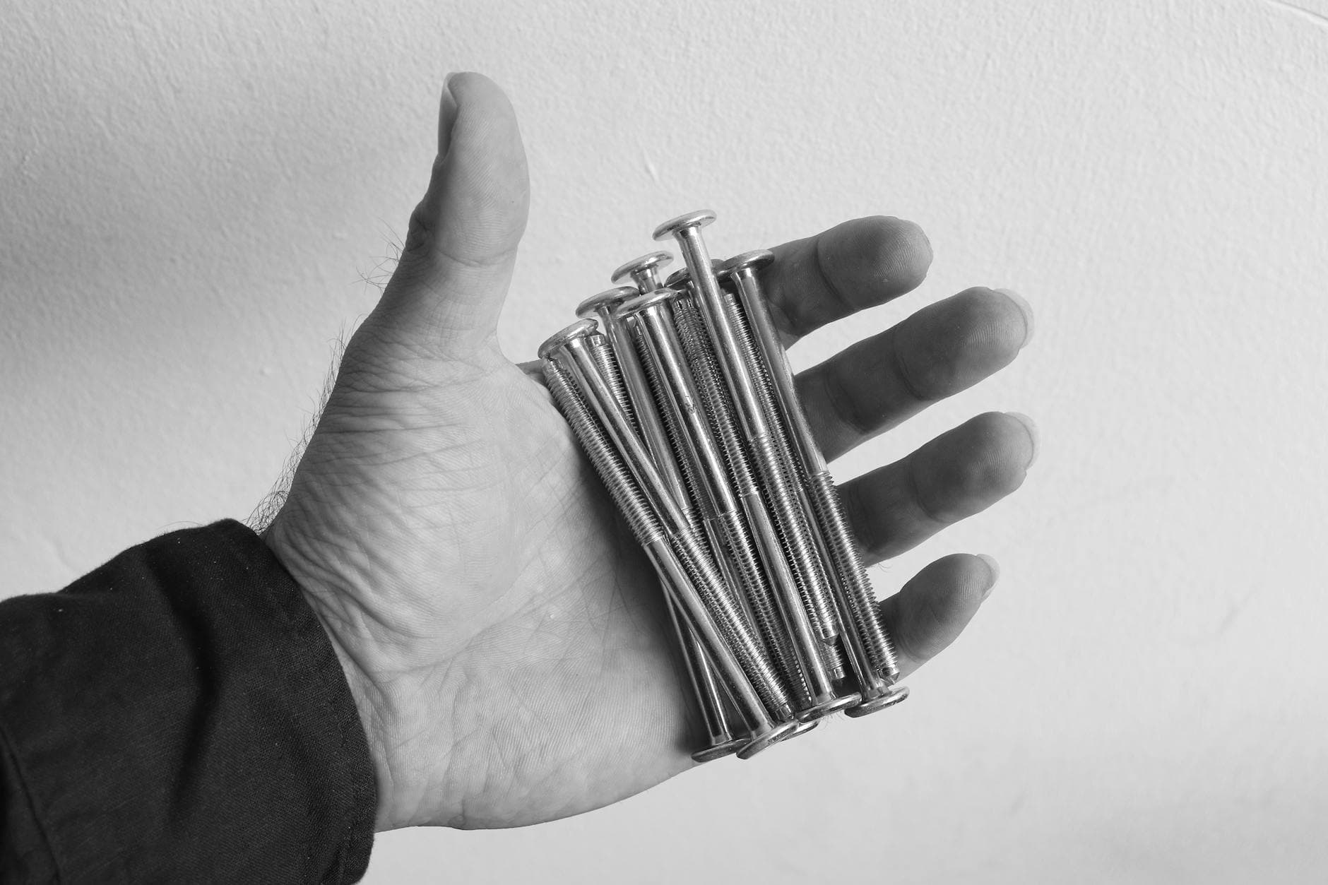 Black and white image of a hand holding several metal screws, showcasing industrial tools.