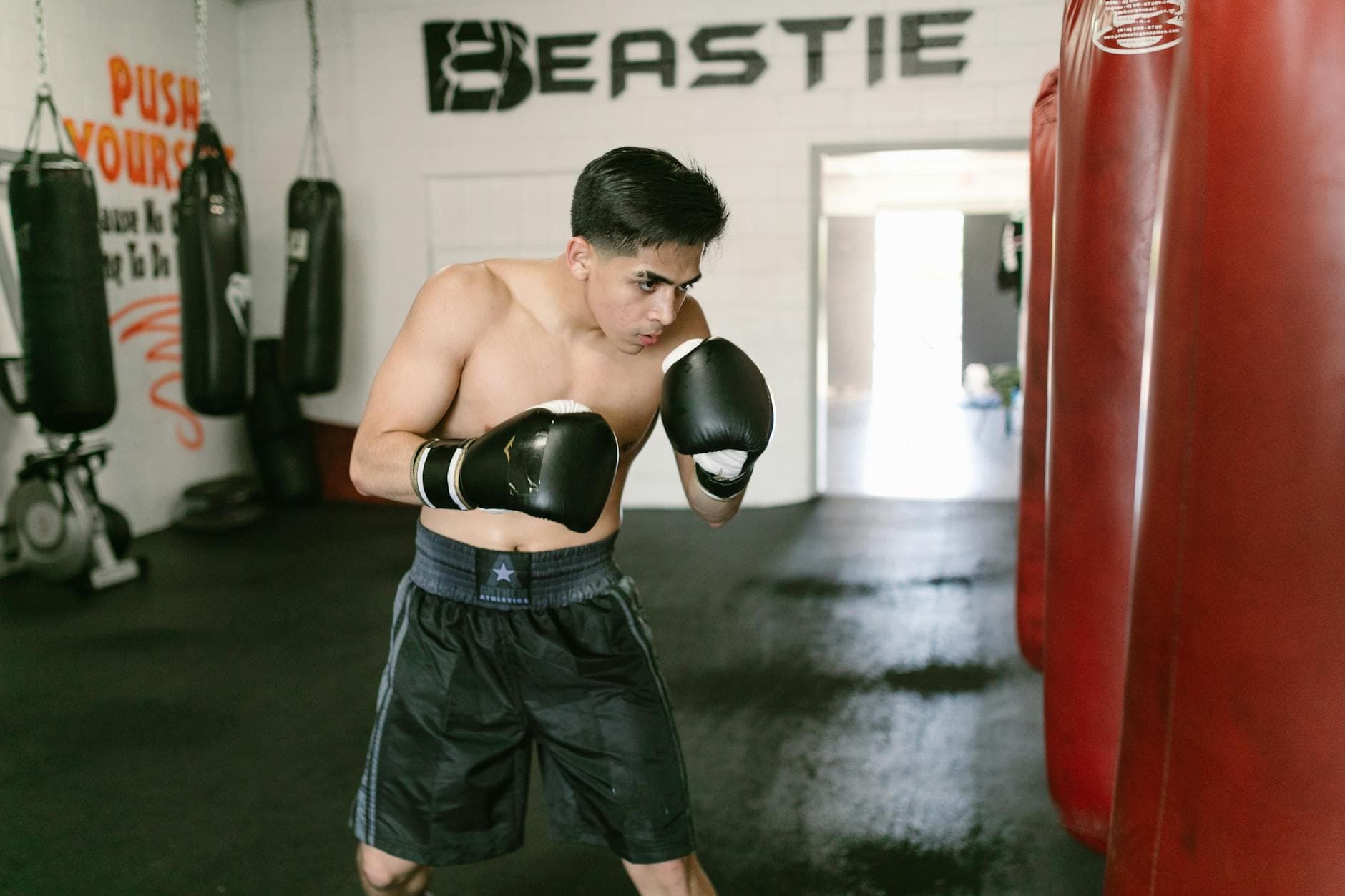 Focused young boxer practicing punches with a heavy bag in a boxing gym.