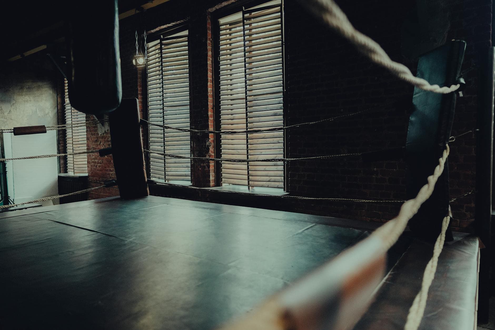 Empty boxing ring in an atmospheric gym with moody lighting and brick walls.