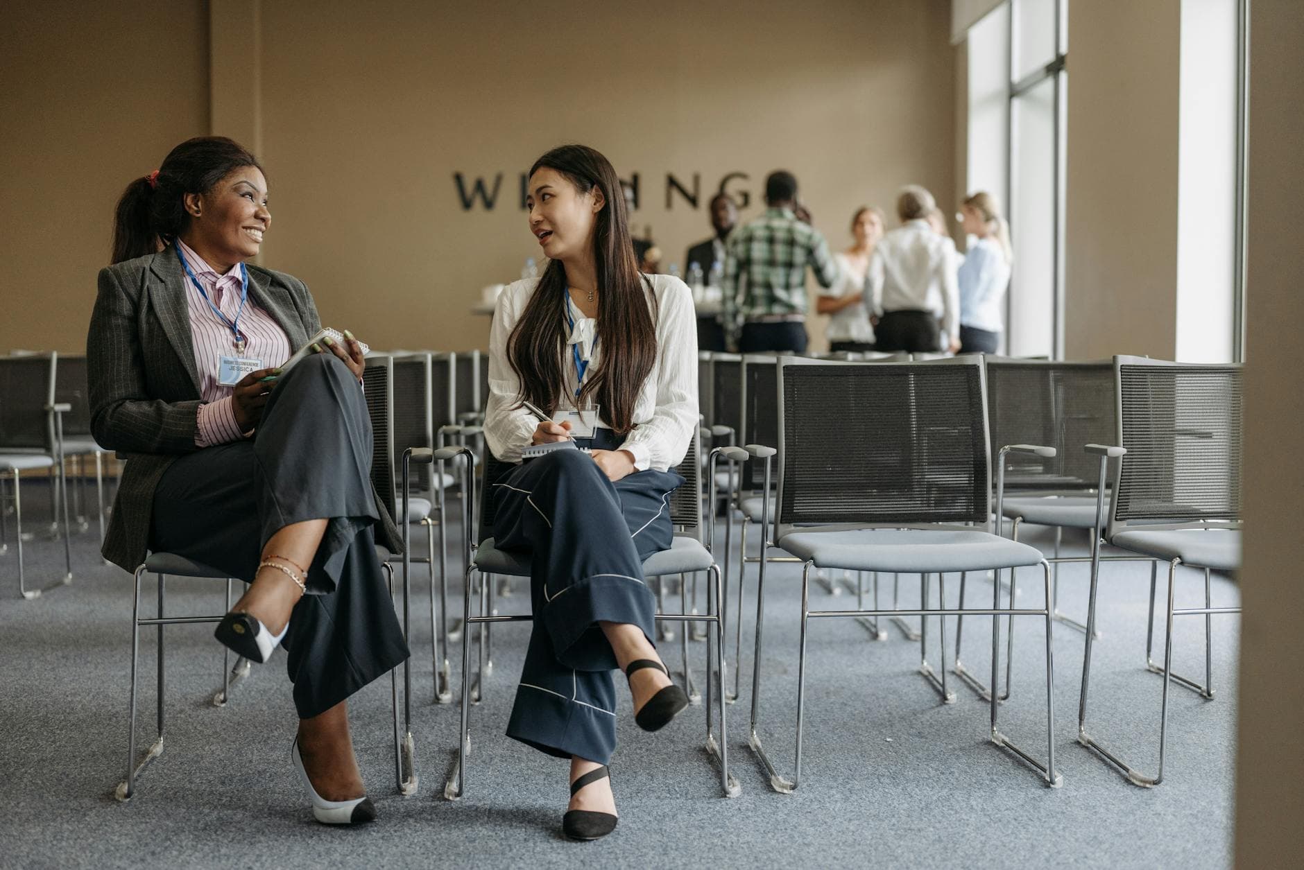 Two businesswomen talking during a conference break, showcasing teamwork.