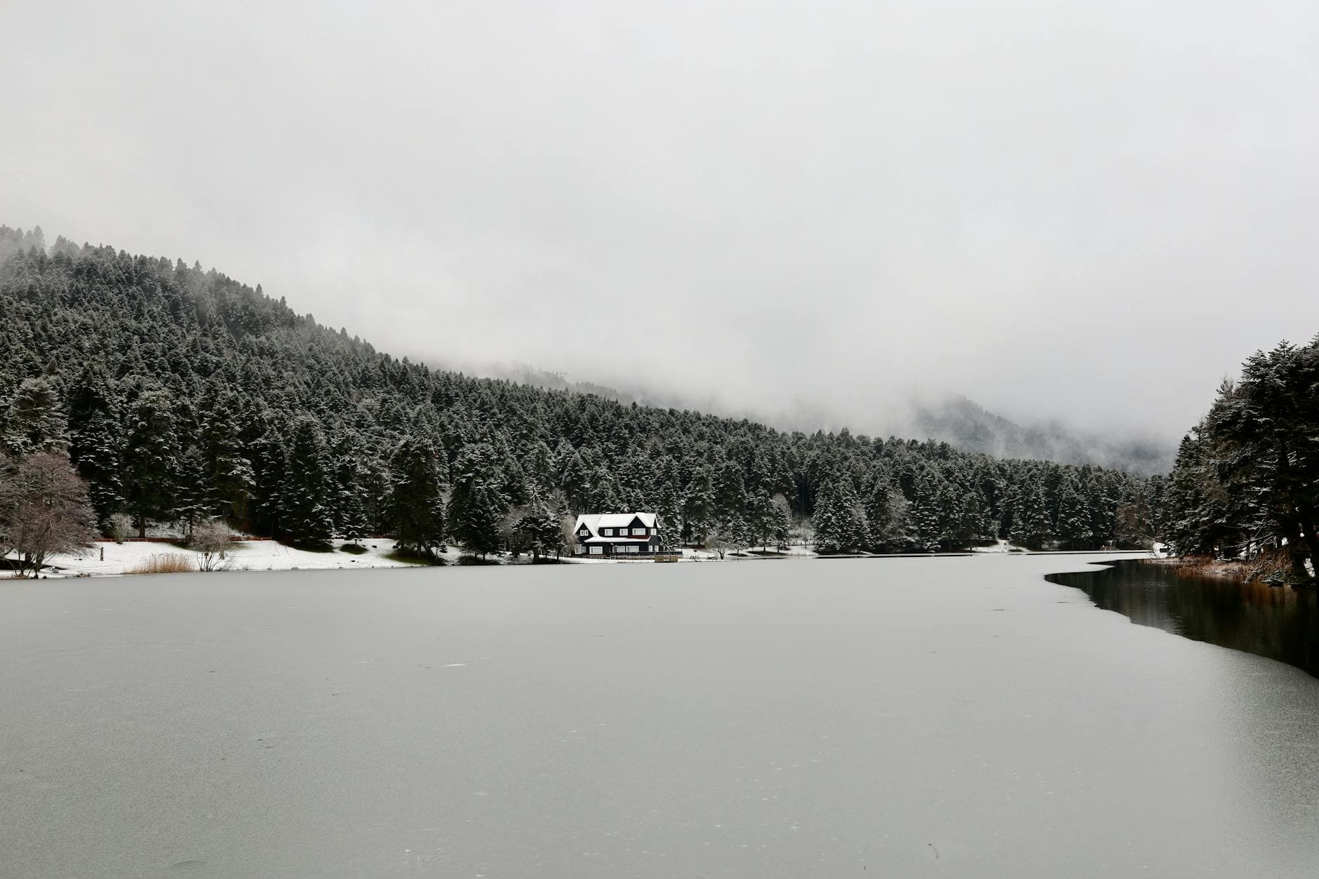 A tranquil winter scene with a cabin by a frozen lake surrounded by snow-covered trees in Gölcük Köy, Turkey.