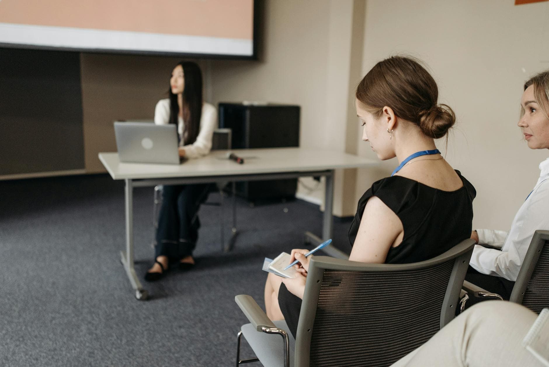 Attendees taking notes during a professional business conference indoors, focused on presentation.