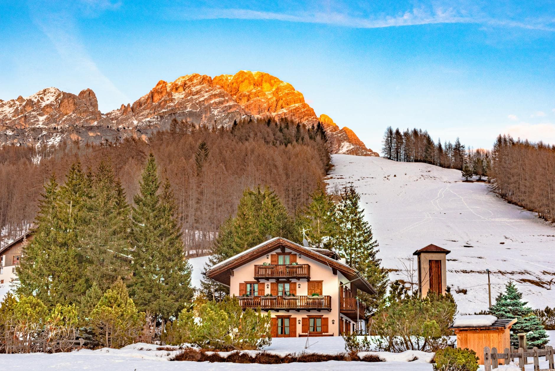 Scenic view of a winter chalet in Cortina d'Ampezzo, Italy with snowy mountains at sunset.