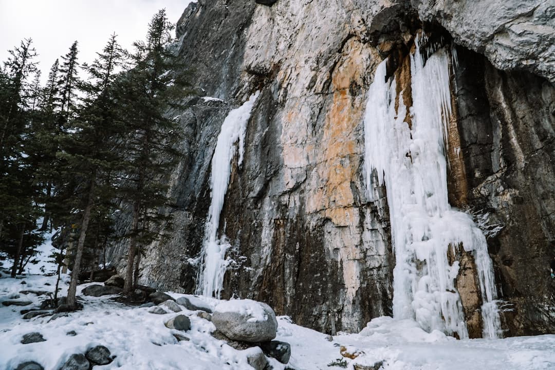 a man standing next to a waterfall in the snow