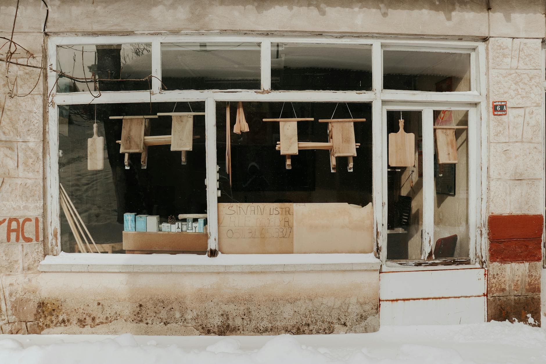 A decaying shop facade with wooden window displays in a snowy city environment.
