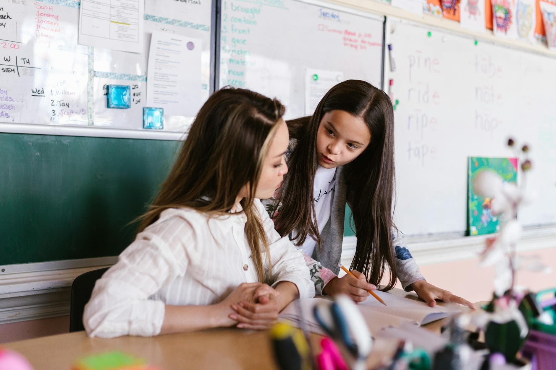 A teacher and student working together at a desk in a classroom setting.