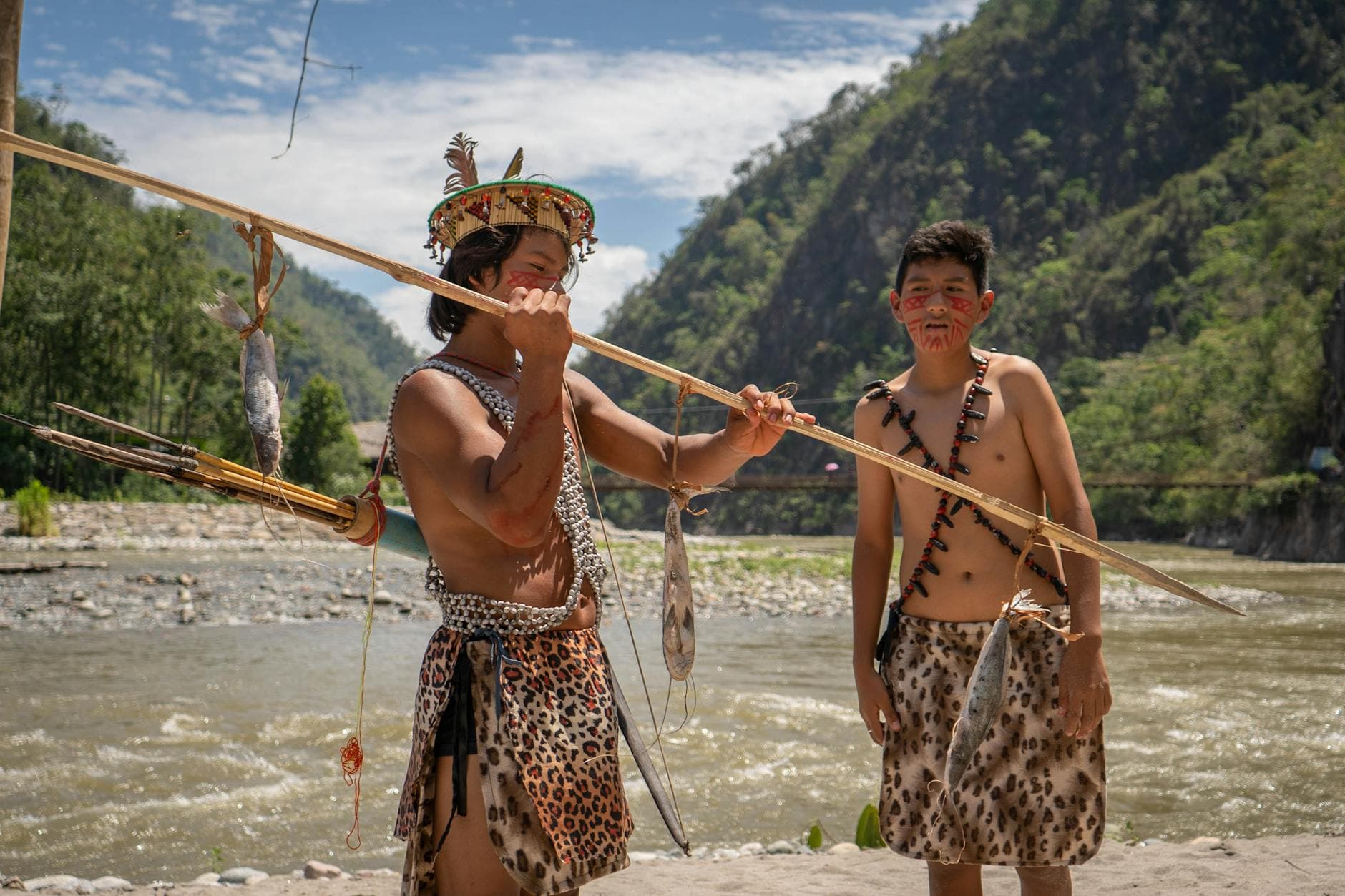 Two indigenous men in traditional attire fish by a river in Peru.