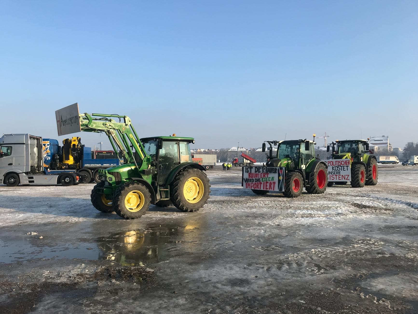 Tractors on a cold winter day with banners protesting, parked on an icy lot.