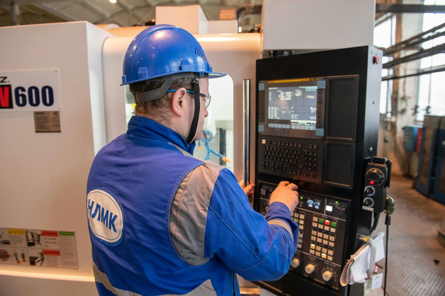 Russian factory worker in blue uniform operating CNC machine indoors.