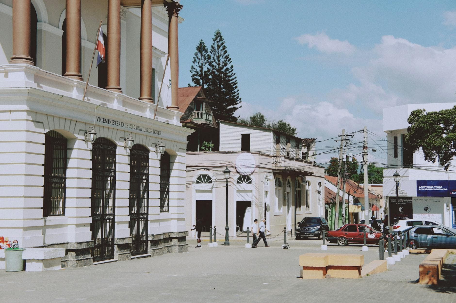 Bustling urban street with historic columns and people walking by classic buildings.