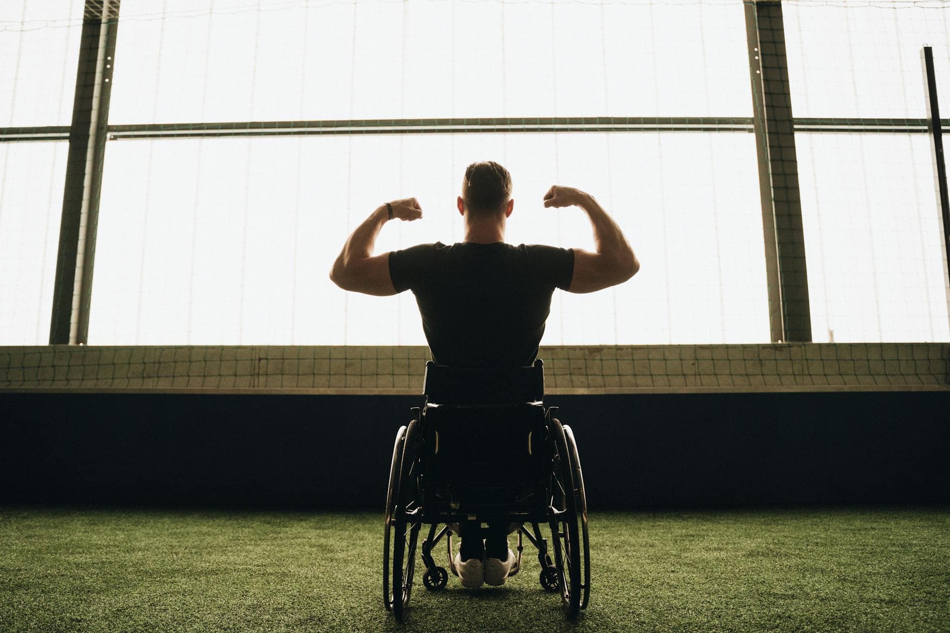 Rear view of a muscular man in a wheelchair flexing in a sports facility.