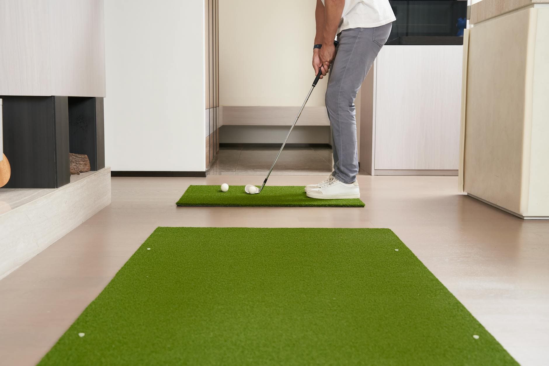 Man practicing putting on an artificial turf mat indoors for golf training.