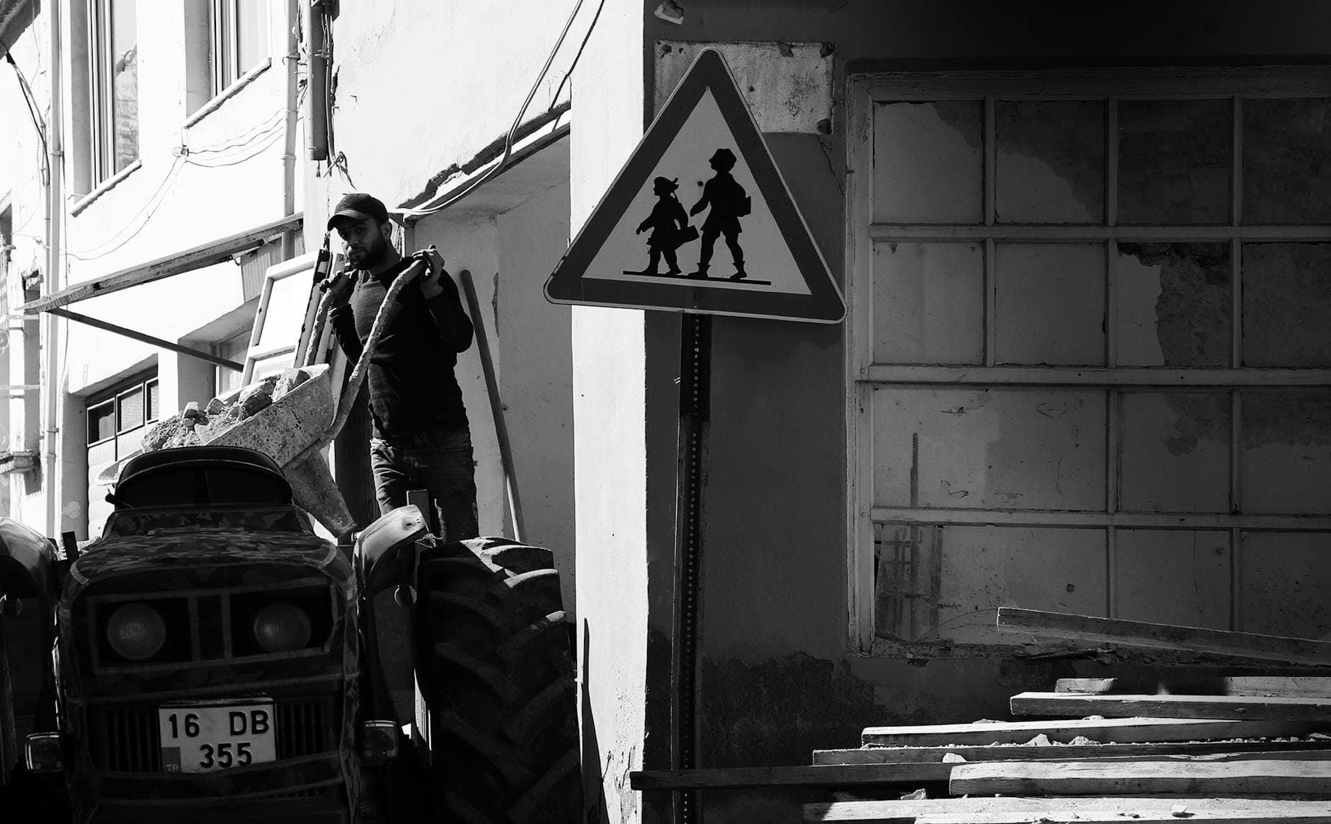 Black and white image of a worker with a tractor at a construction site, featuring a road sign.