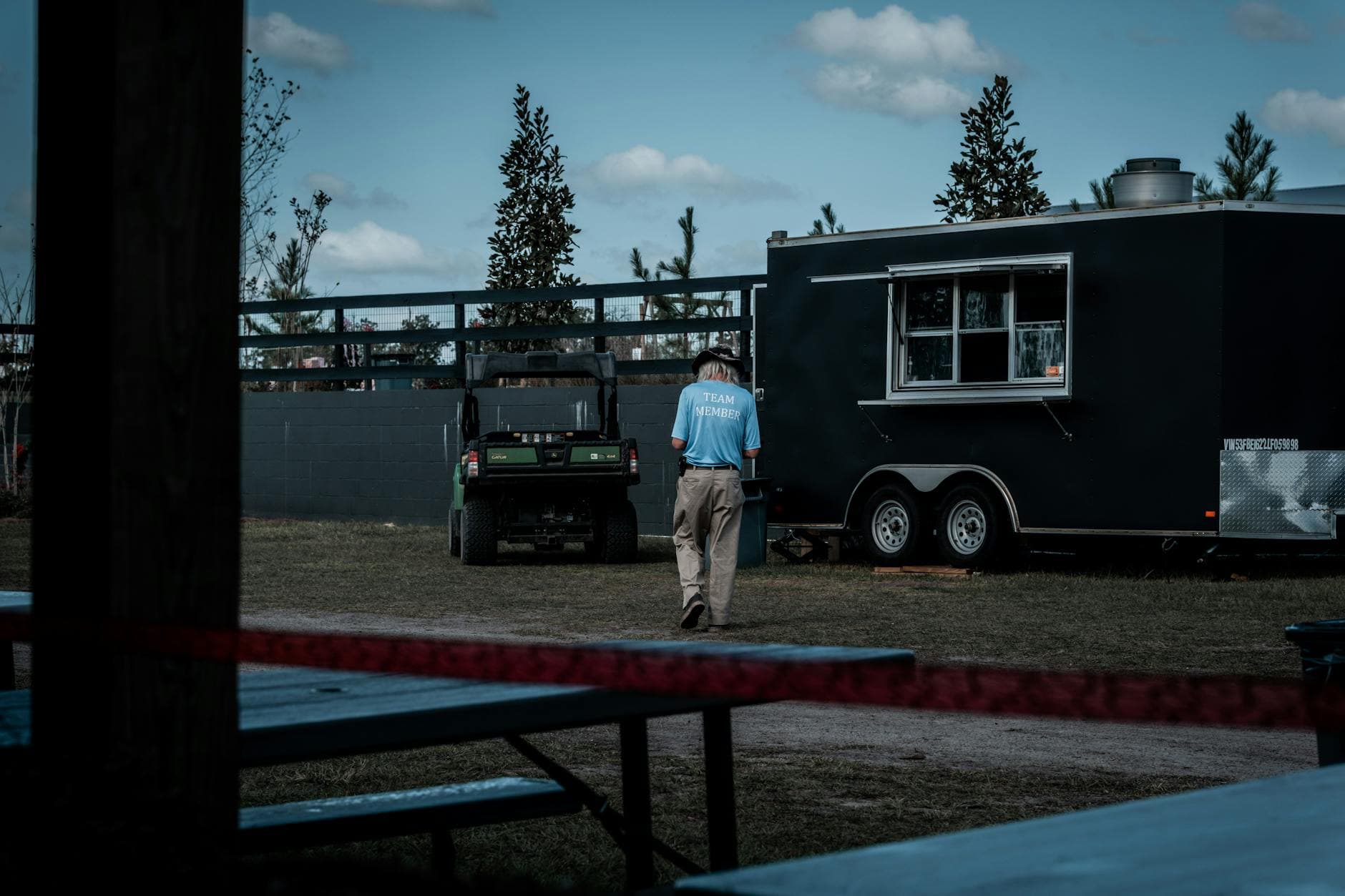 Back view of a man walking towards a black food truck at an outdoor venue under clear blue skies.