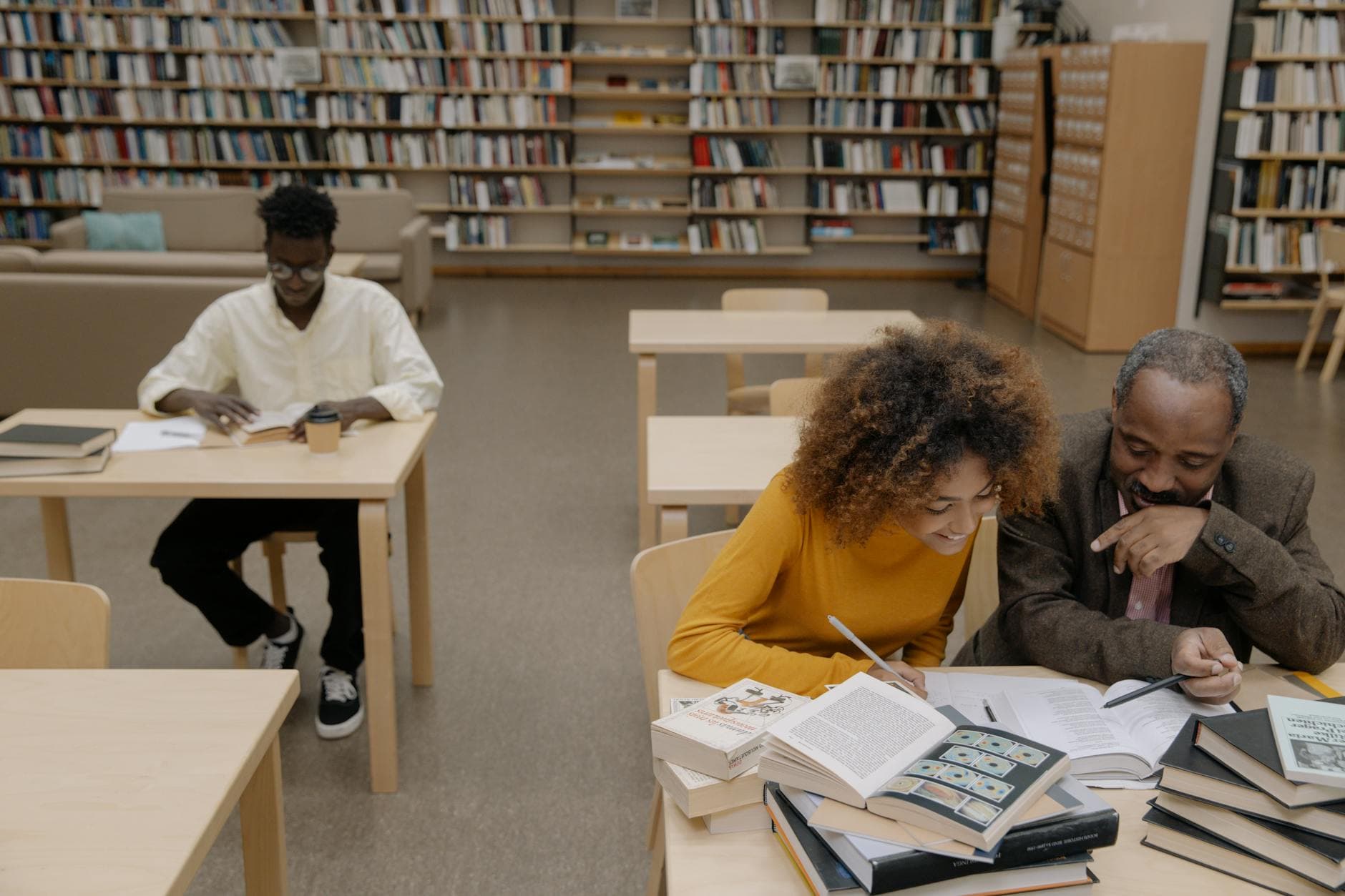 Adults studying together in a library, surrounded by books, promoting learning and diversity.
