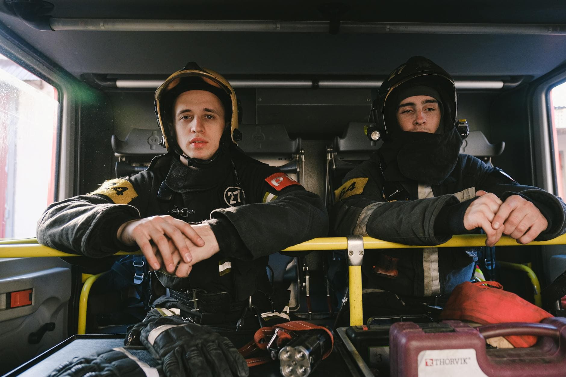 Two firefighters in uniform seated inside a fire truck, ready for action.