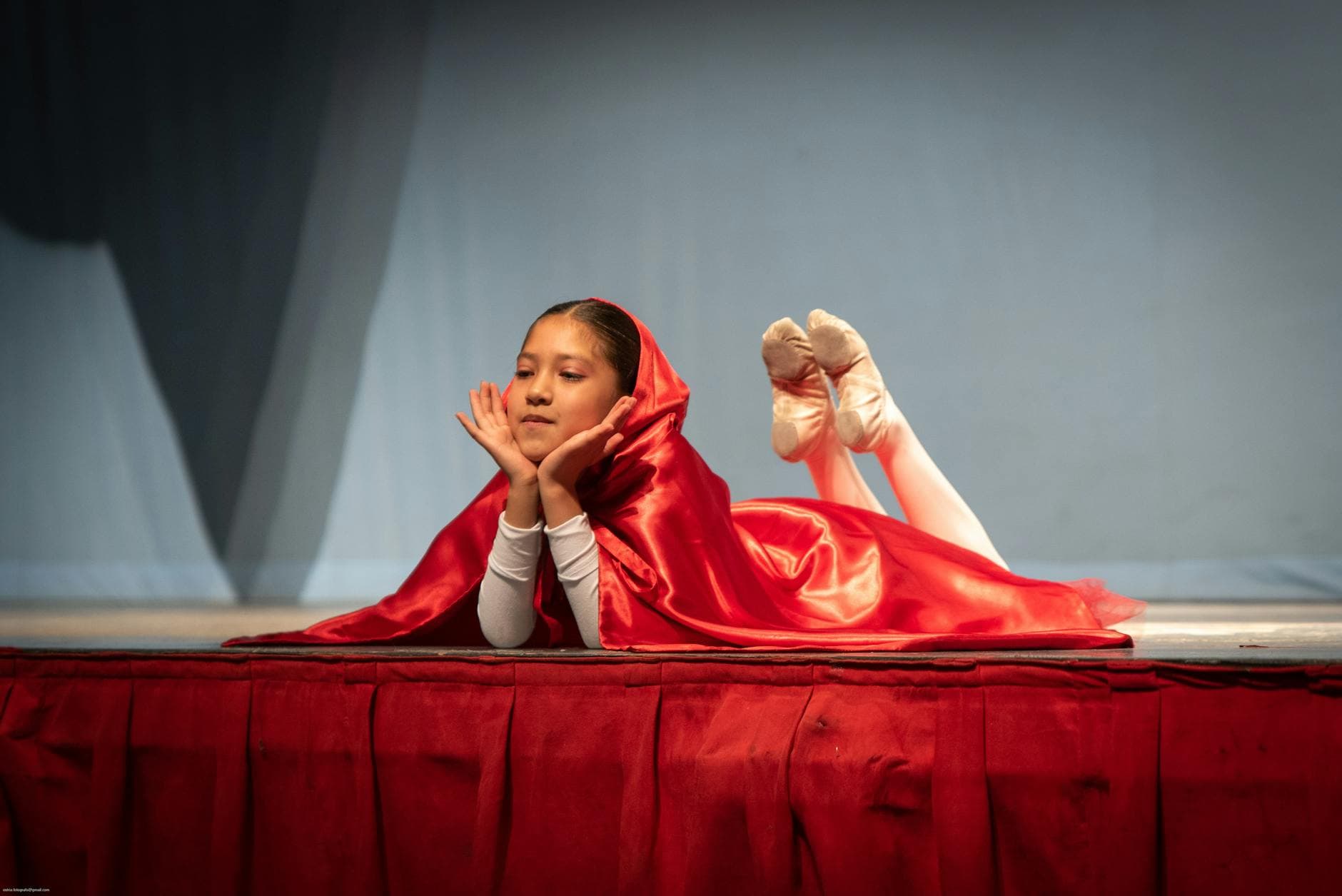 Child performer in Little Red Riding Hood costume lying on stage during a school play.