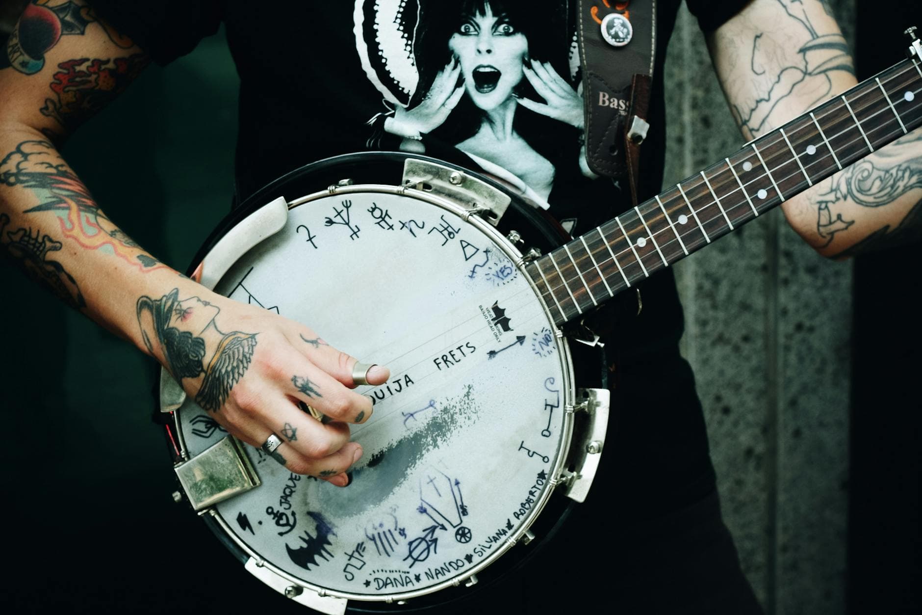 Close-up shot of a tattooed musician playing a unique banjo with custom artwork and symbols.