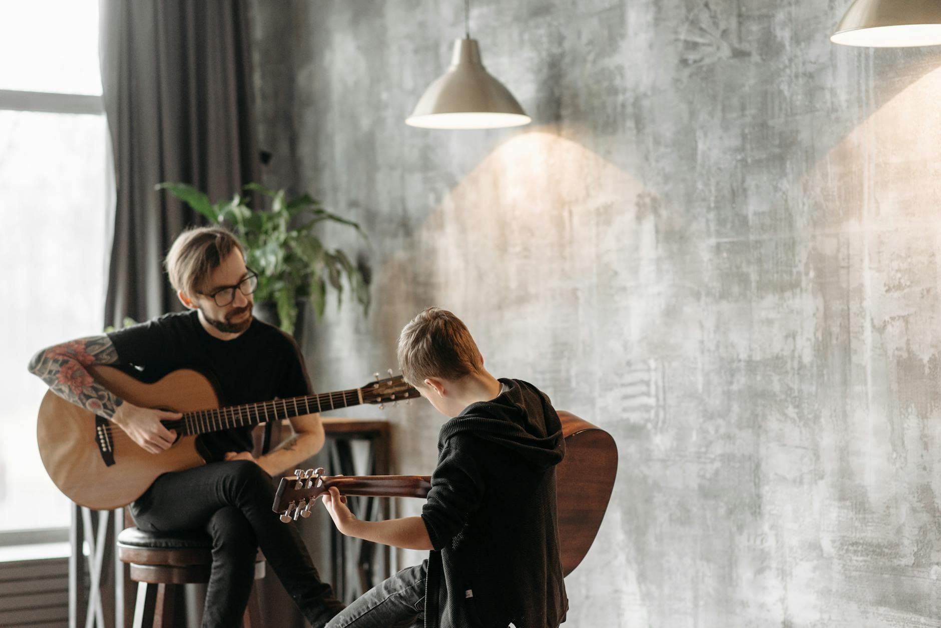 A man and a boy engaged in a guitar lesson, playing acoustic guitars indoors.