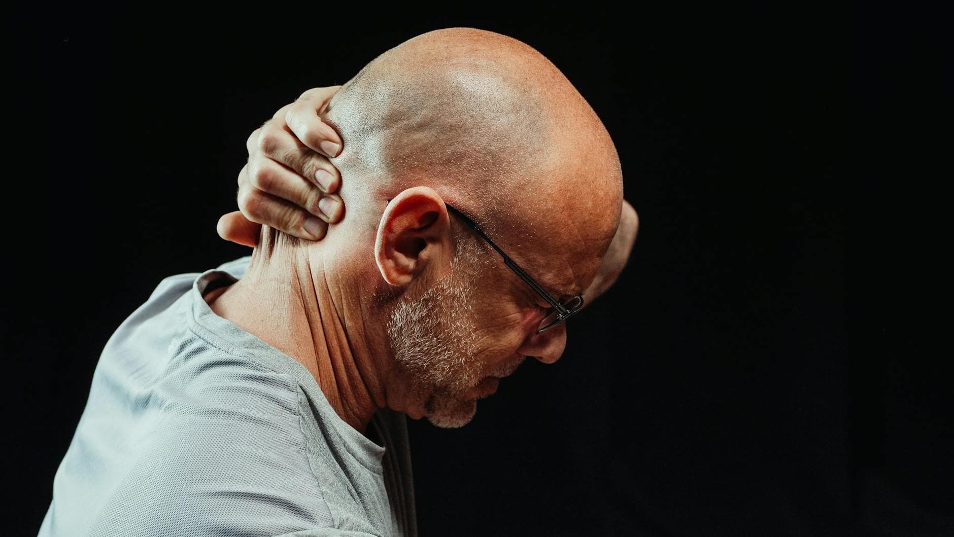 Side view of a man holding his neck in pain against a black background.