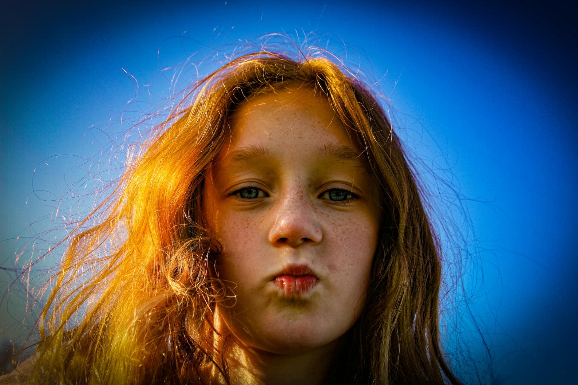 Close-up portrait of a redheaded girl with freckles against a vivid blue background.
