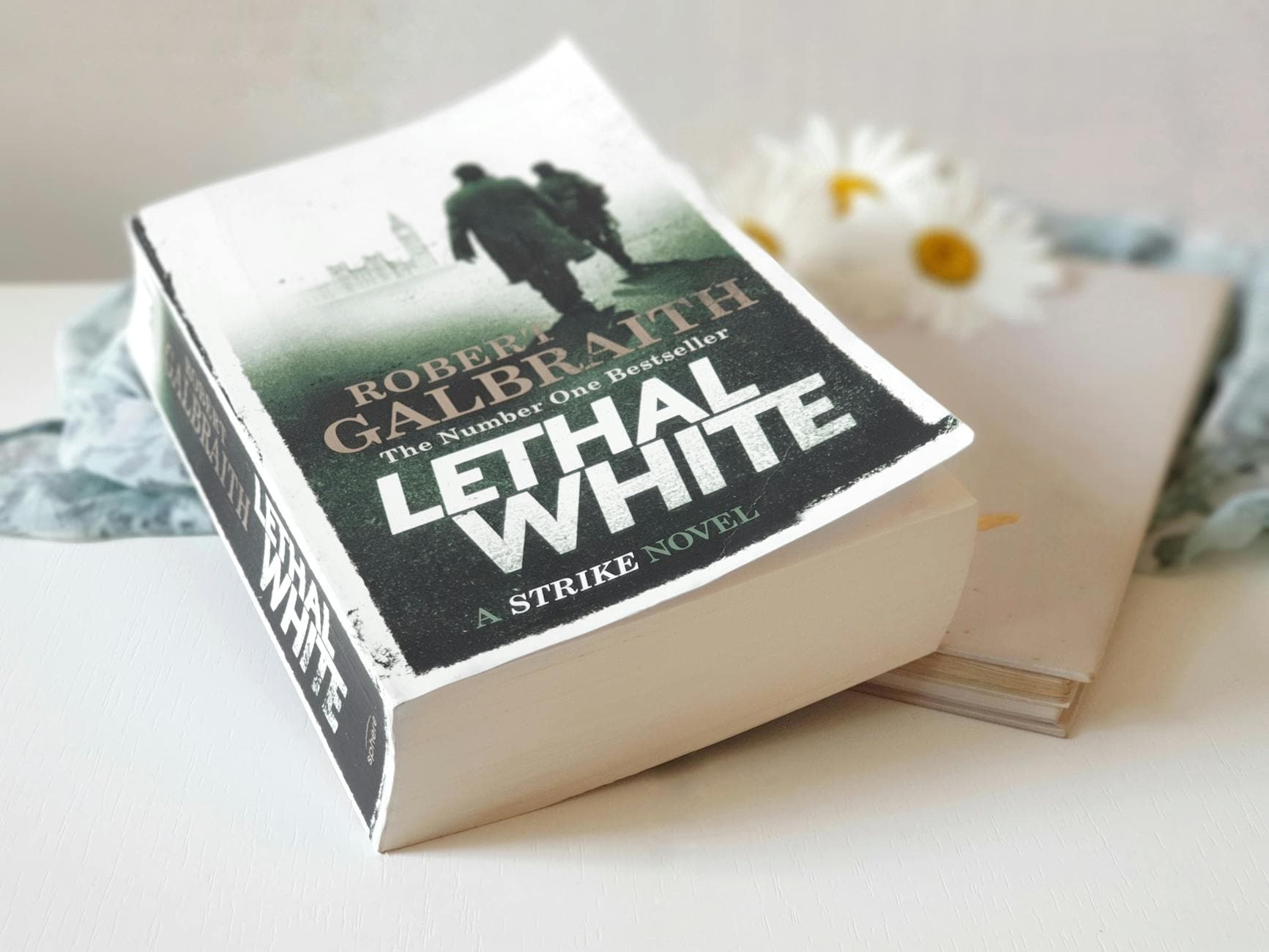 Close-up of the novel 'Lethal White' resting on a table near daisies.