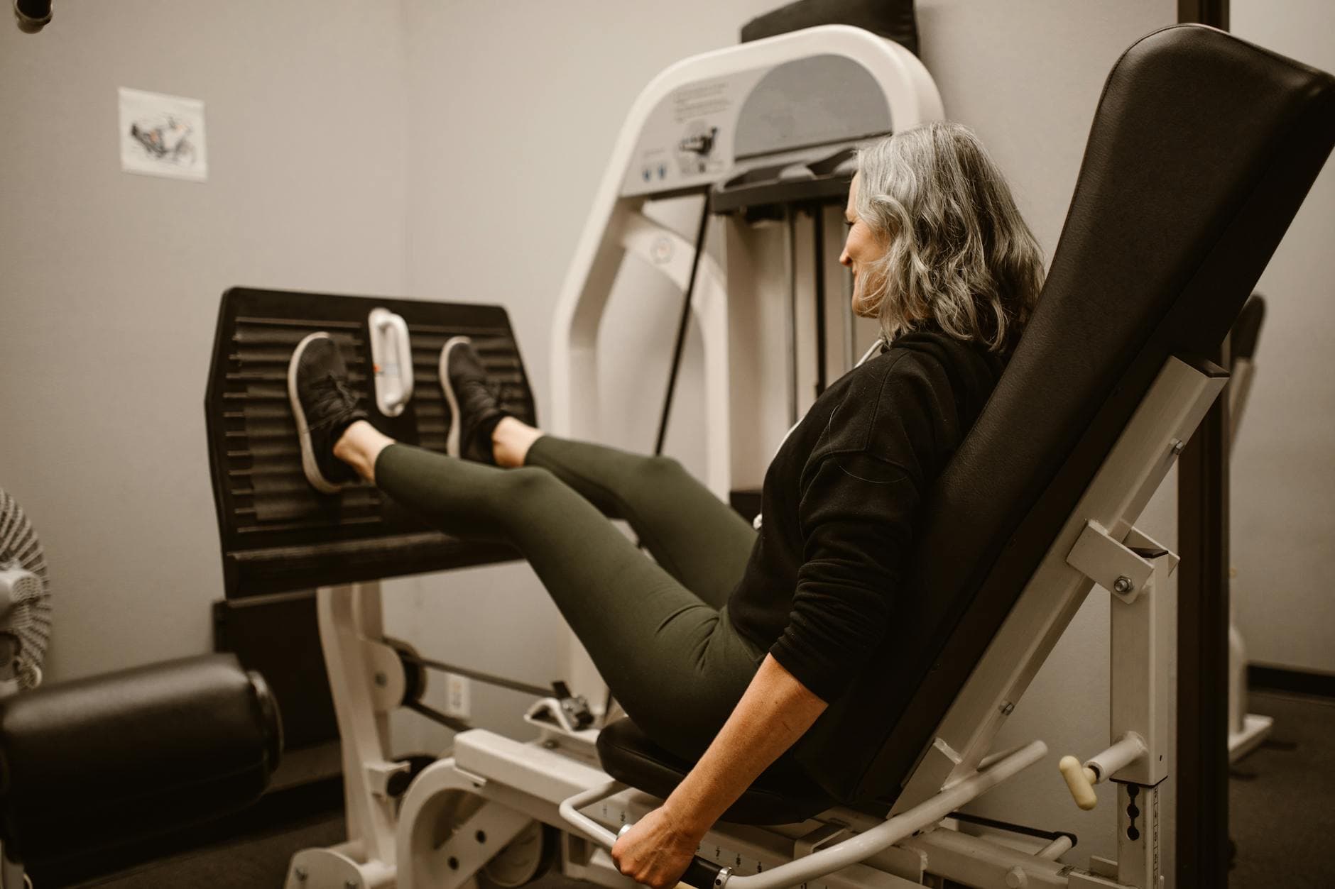Mature woman working out on a leg press machine in a gym, promoting active and healthy lifestyle.
