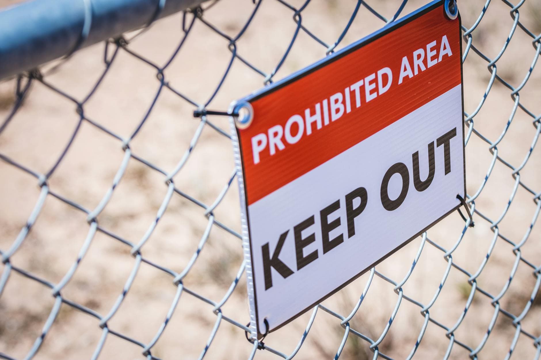 Close-up of a 'Prohibited Area' and 'Keep Out' sign on a chain link fence.