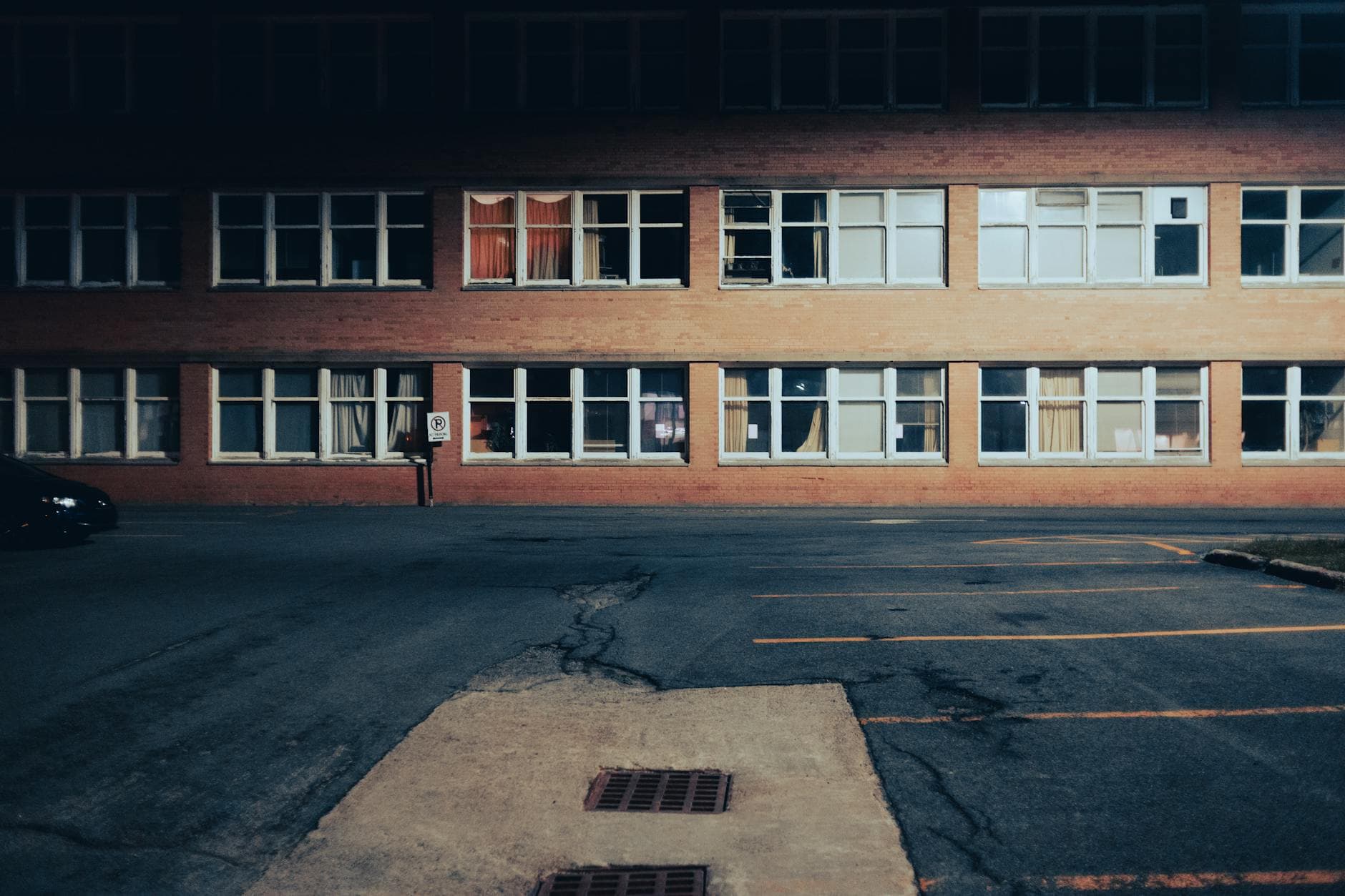 Desolate parking lot by a brick building at night, highlighting urban solitude.