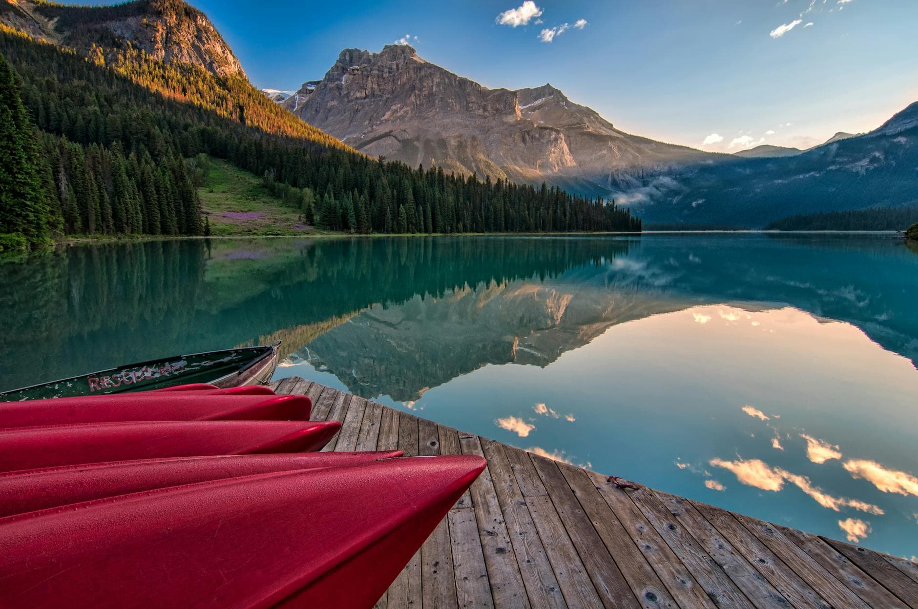 Vibrant red canoes on Emerald Lake with stunning mountain reflections at sunrise in British Columbia.