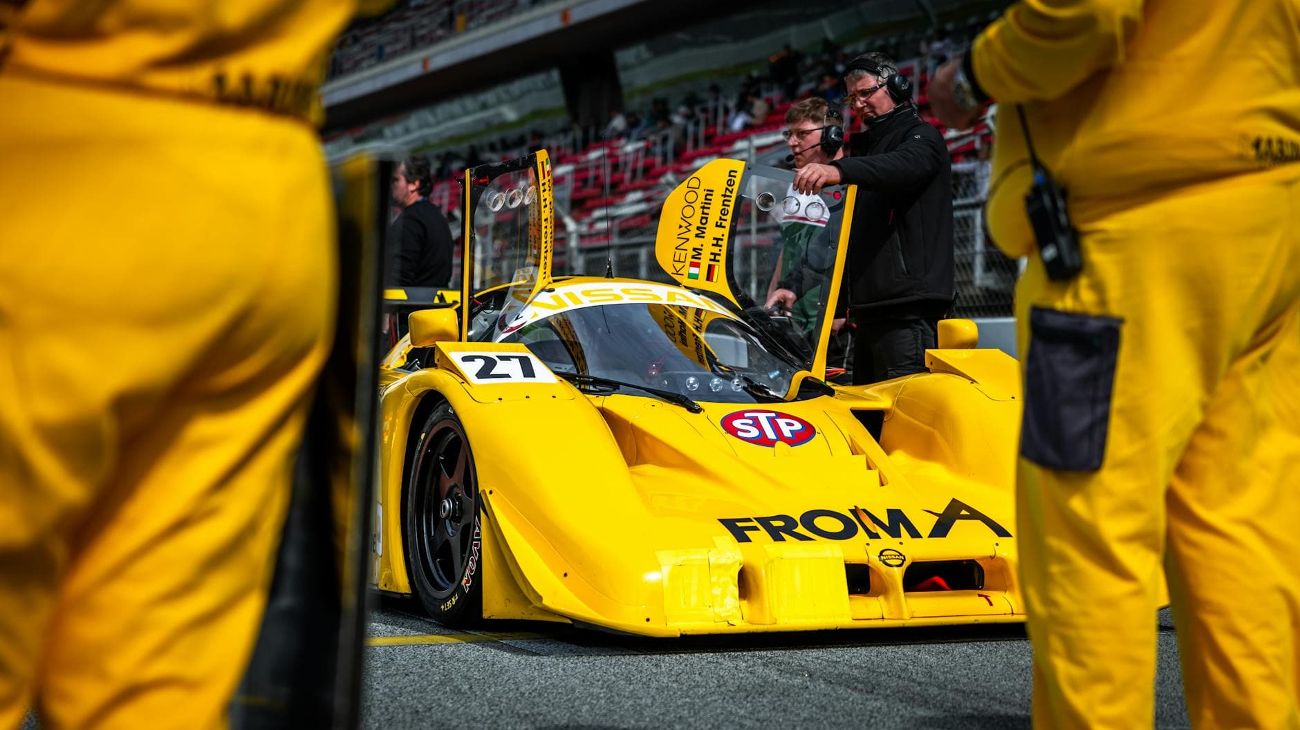 Bright yellow race car on track, surrounded by crew, ready for start.