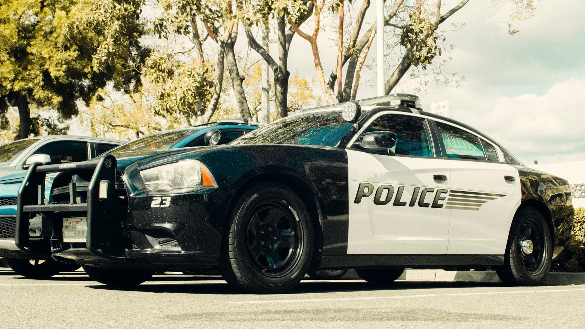 Black and white police car parked outdoors with trees in the background.