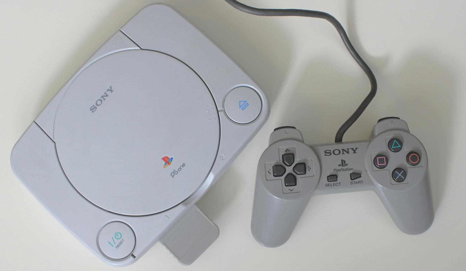 Top view of a classic Sony PlayStation console with a controller on a white surface.