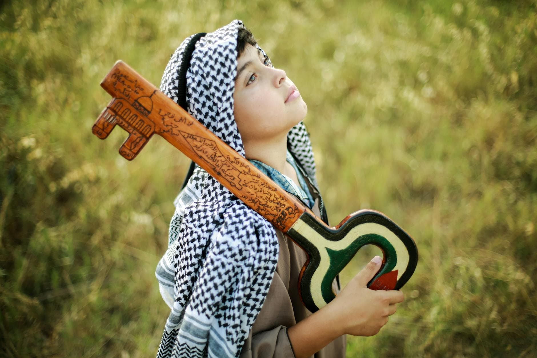A thoughtful Palestinian child holds a symbolic key, representing heritage and hope, in an outdoor setting.