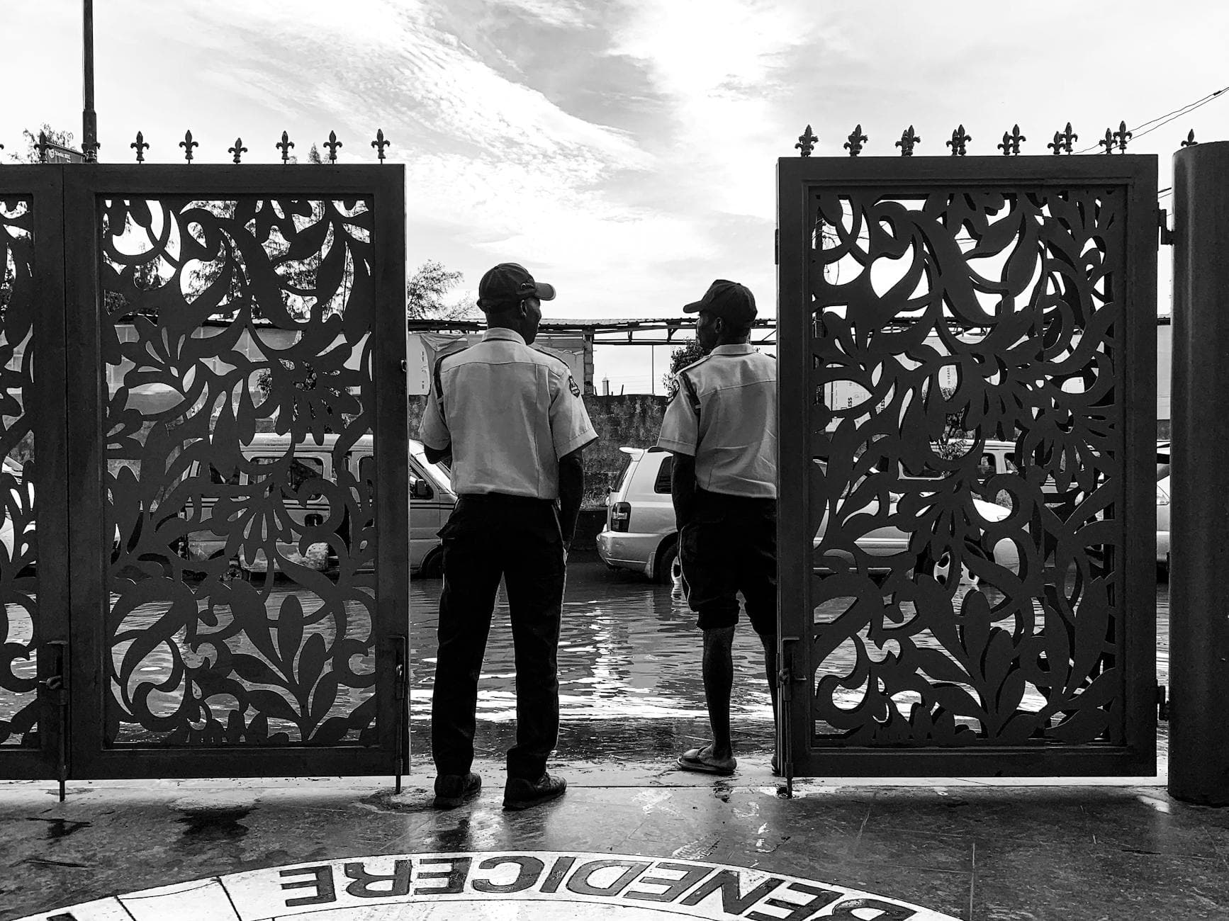 Black and white photo of two security guards standing by a decorative gate.