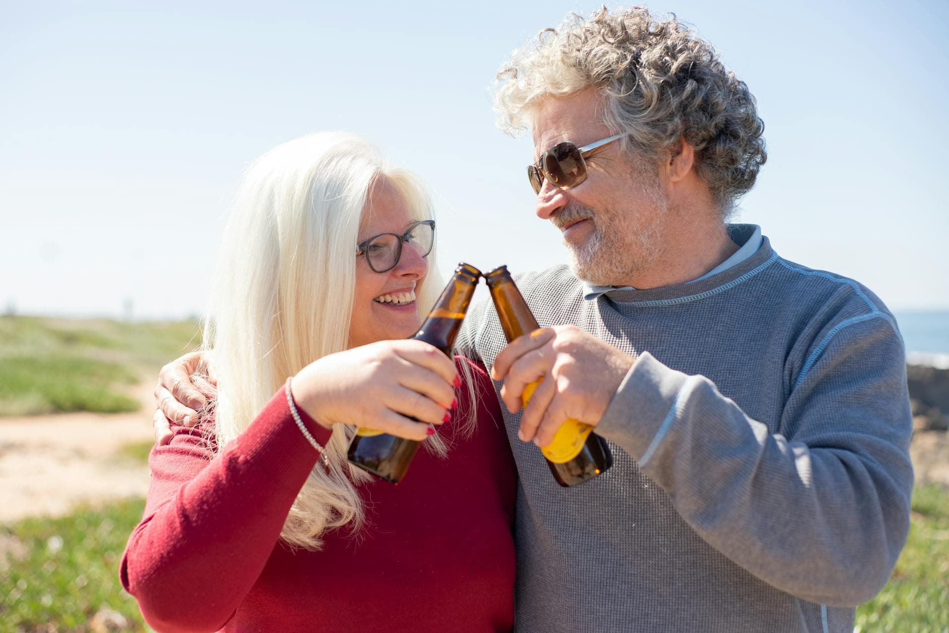 Senior couple enjoying a sunny day outdoors, toasting with beer bottles, embodying joy and companionship.