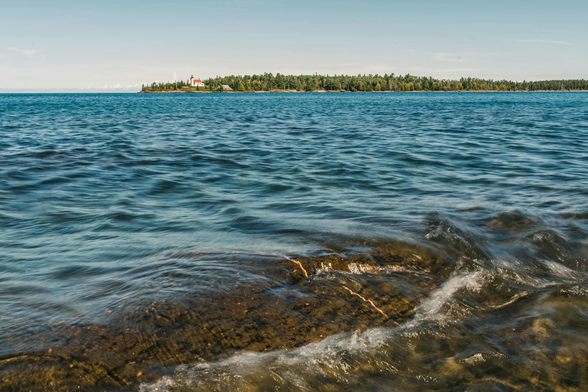 Distant view of Copper Harbor Lighthouse with rocky shoreline in Michigan.