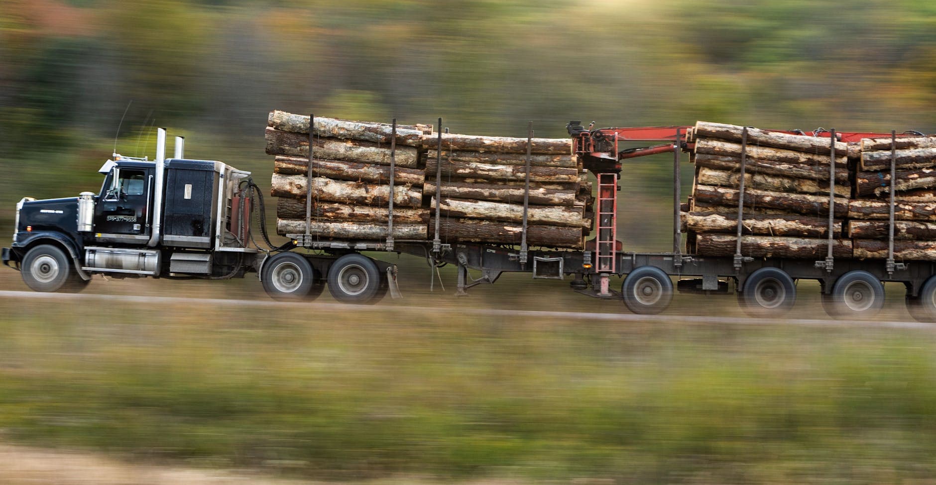 A logging truck transports timber swiftly along a rural highway.