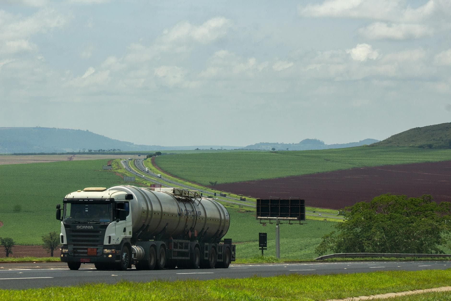 A large truck drives through picturesque countryside with vast agricultural fields.