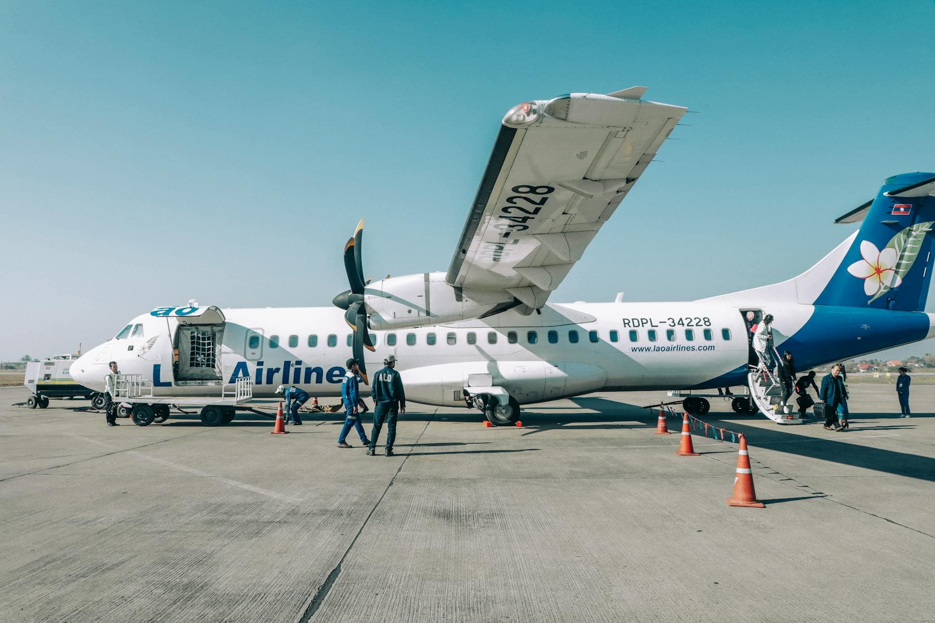 Passengers boarding an airplane at Vientiane's Don Noun Airport during a sunny day.