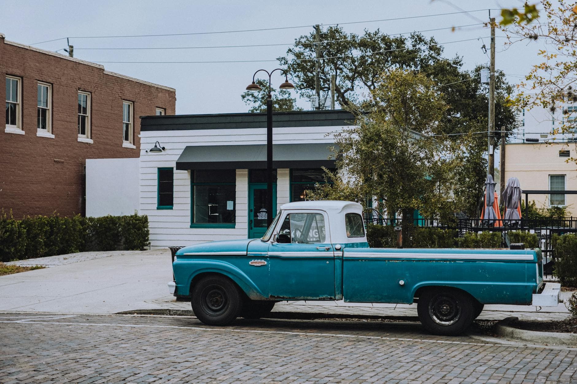 A classic blue Ford truck parked on a cobblestone street in a quaint urban area.